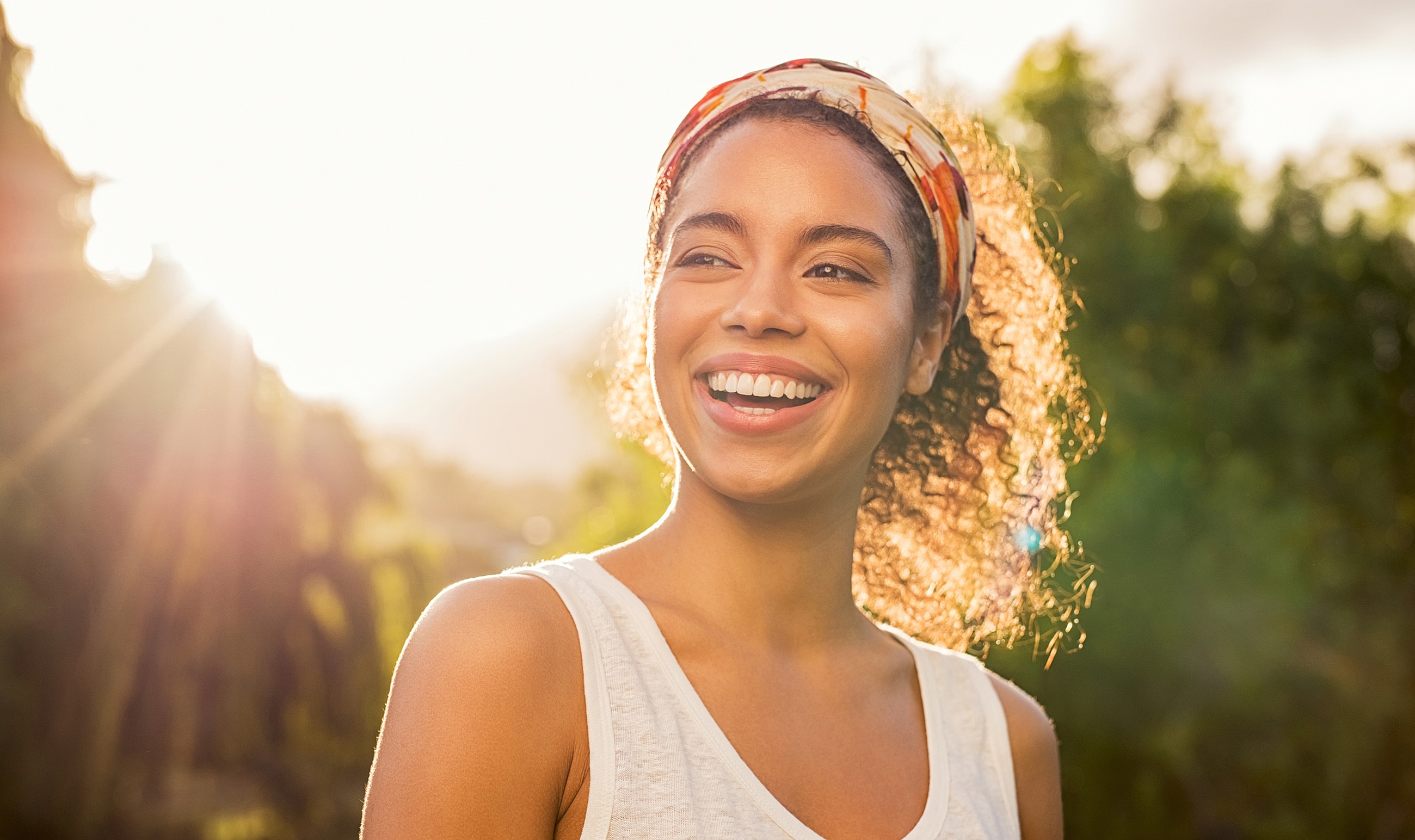 Smiling woman with curly hair in sunlight.