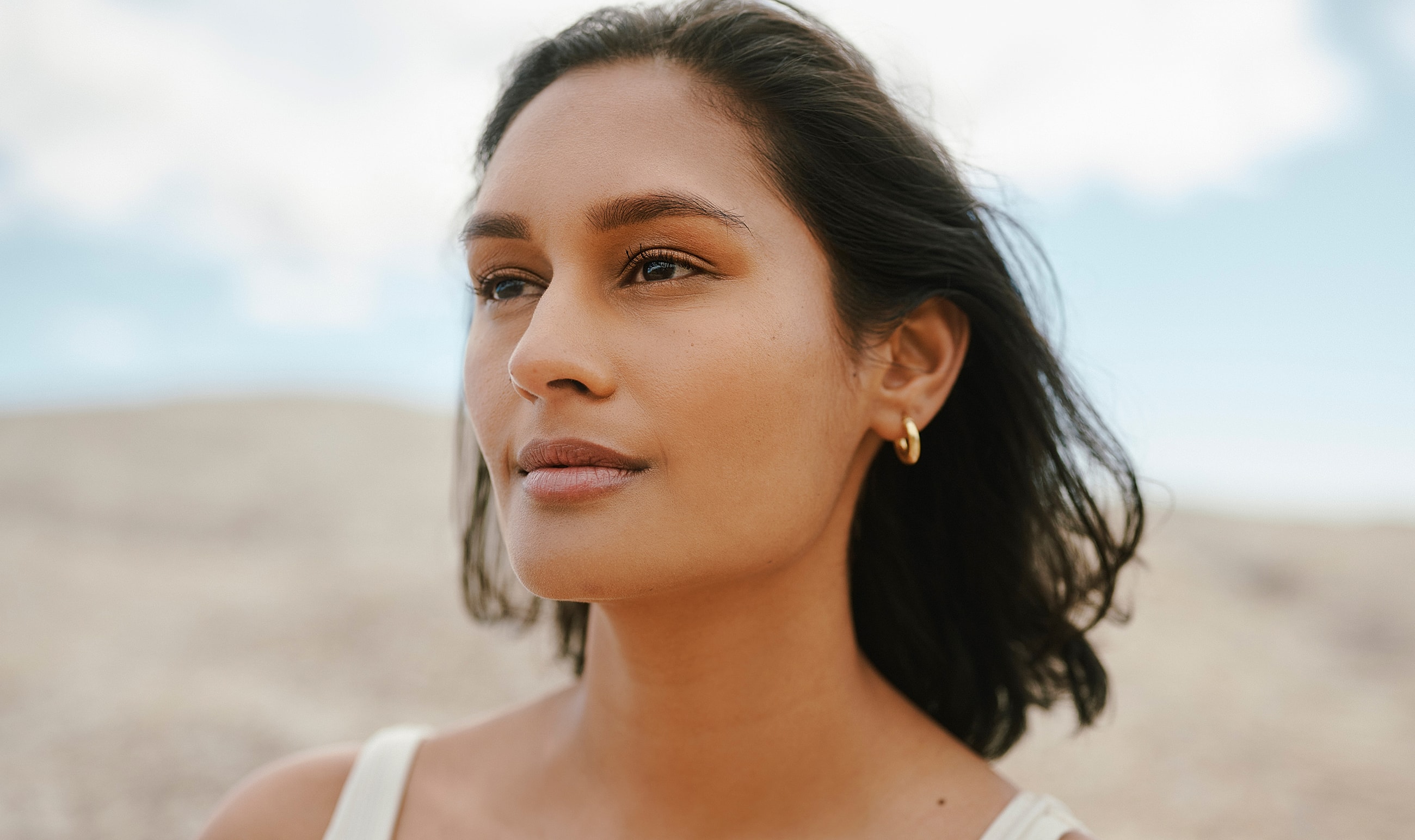 Woman with short hair outdoors, looking thoughtfully.